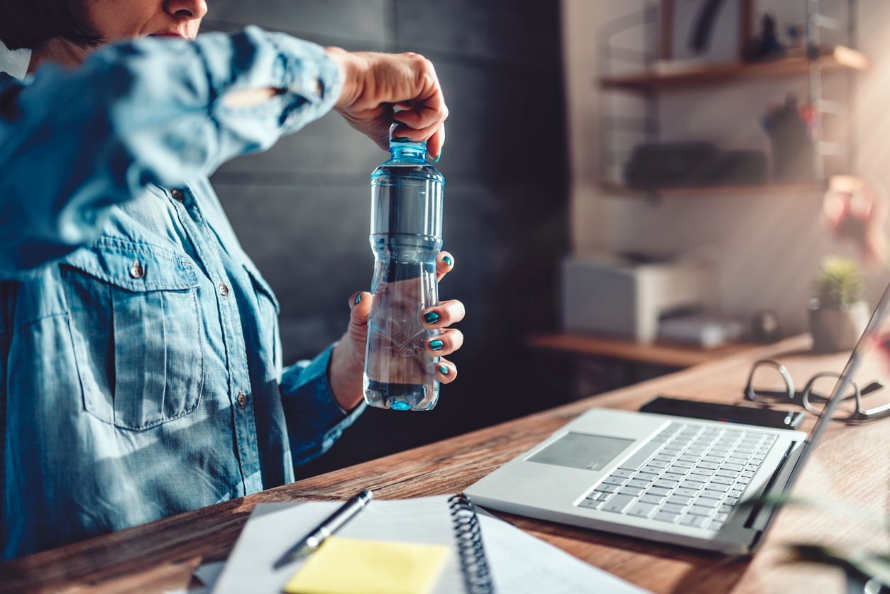 Woman wearing denim shirt working in the office and opening plastic bottle of water workplace wellness