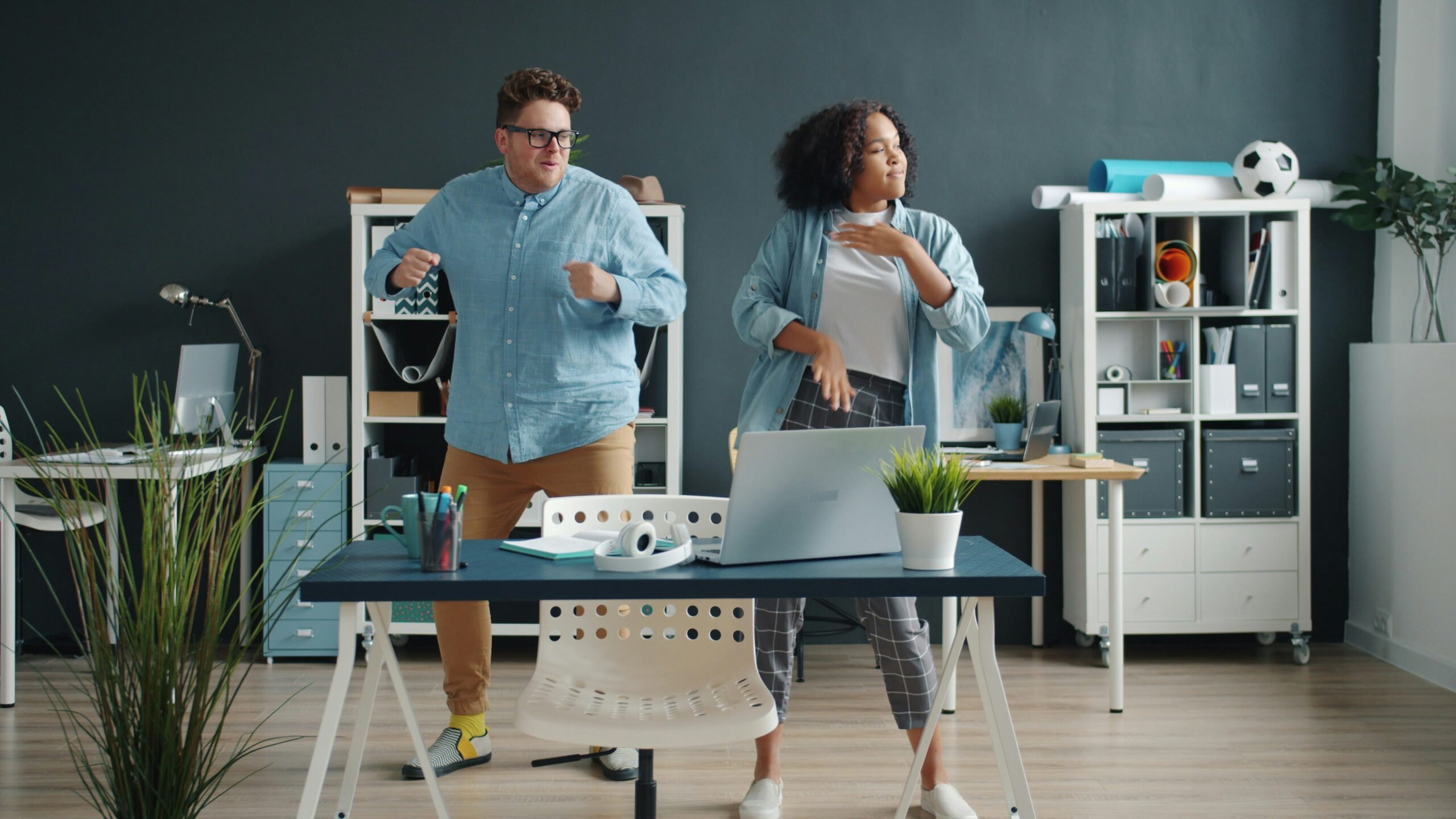 Mixed race office workers girl and guy are having fun together dancing enjoying music relaxing at work. Entertainment, joyful people and modern lifestyle concept. workplace wellness