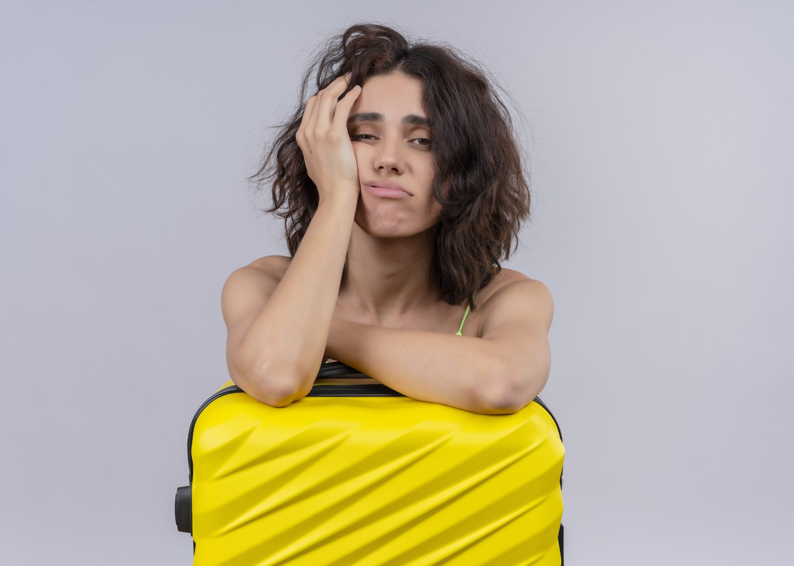 tired young beautiful traveler girl putting arms on suitcase and putting hand on cheek on isolated white background