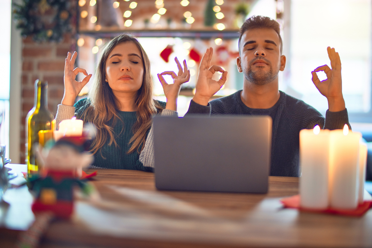 holiday stress relief Young beautiful couple sitting using laptop around christmas decoration at home relax and smiling with eyes closed doing meditation gesture with fingers. Yoga concept. holiday stress for couples