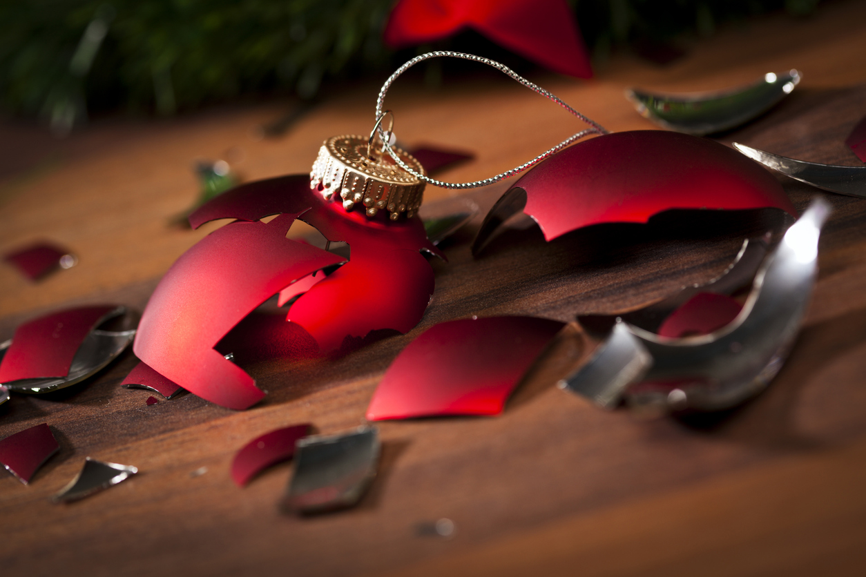 broken red christmas bauble and shards on wooden floor holiday stress for couples