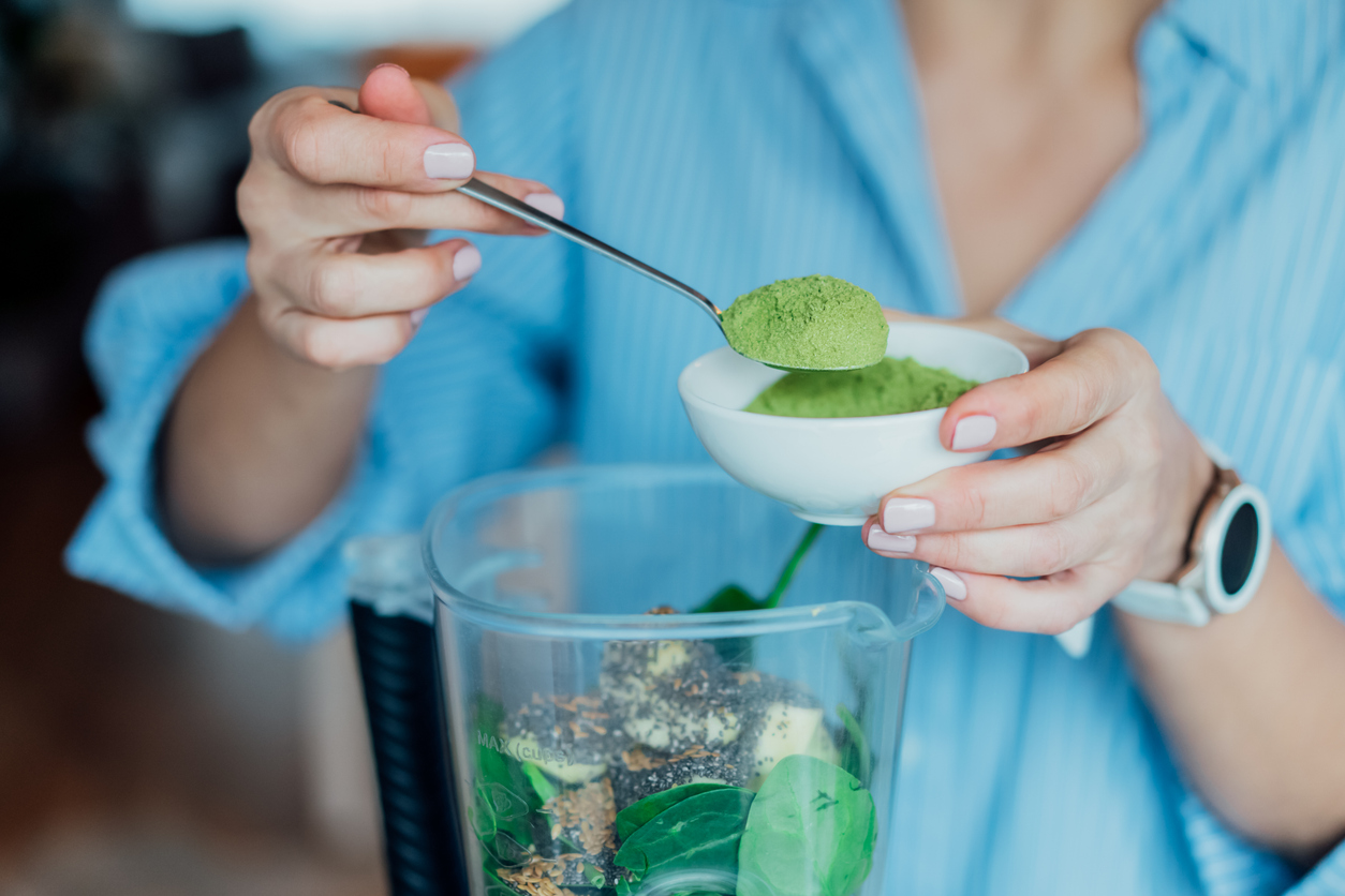 cycle syncing superfoods for energy winter smoothie Close up woman adding wheat grass green powder during making smoothie on the kitchen. Superfood supplement. Healthy detox vegan diet. Healthy dieting eating, weight loss program. Selective focus.